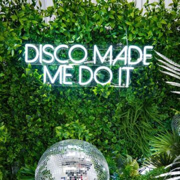 disco made me do it neon sign on greenery wall