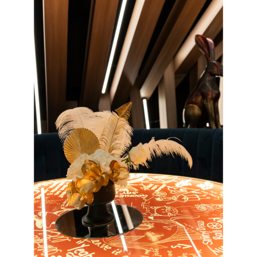 White and gold floral arrangement with ostrich feathers, gold foliage and artificial flowers styled on a glowing cocktail table for luxury event décor.