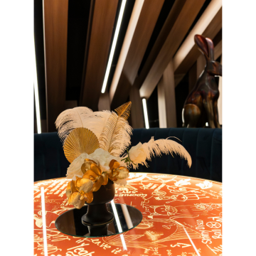 White and gold floral arrangement with ostrich feathers, gold foliage and artificial flowers styled on a glowing cocktail table for luxury event décor.