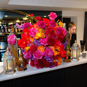 Moroccan Sunset Floral Feature with vibrant artificial flowers, roses, orchids and Moroccan lanterns styled on a wedding bar display for events.