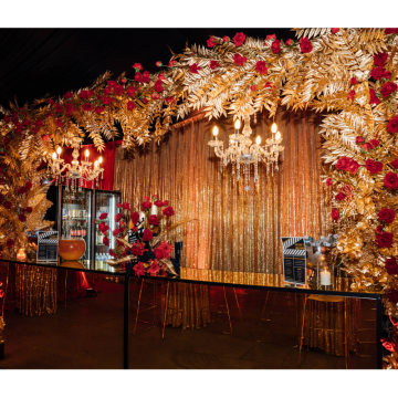 Hollywood Glam floral bar display with gold foliage, red roses, chandeliers and luxury event styling, creating a glamorous cocktail bar feature.