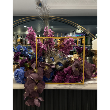 Peacock Masquerade Floral Feature with blue and purple artificial flowers, peacock feathers and a gold cube styled on a luxury event bar display.