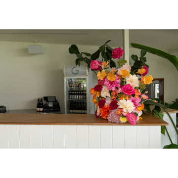 Sunset Fiesta Floral Feature with vibrant orange and pink artificial flowers styled on a modern event bar for colourful wedding and party dÃ©cor.