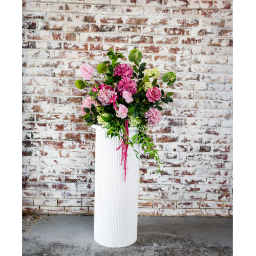 Pink Oasis Floral Feature with pink artificial flowers, lush greenery and faux florals displayed on a white plinth for elegant wedding event styling.