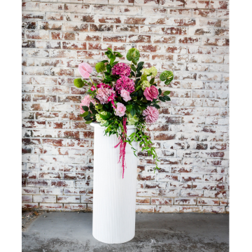 Pink Oasis Floral Feature with pink artificial flowers, lush greenery and faux florals displayed on a white plinth for elegant wedding event styling.